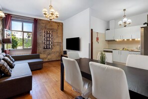 A modern living room with a sofa, dining table, and chairs, a kitchen with white cabinets, and a stone wall with a fire escape mural. - Apartment 'Balcony Porto's' with Balcony, Wi-Fi and Air Conditioning (Porto)