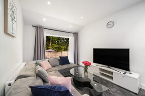 A modern living room with a sofa, a glass coffee table, a flat-screen TV, and a large window with curtains.