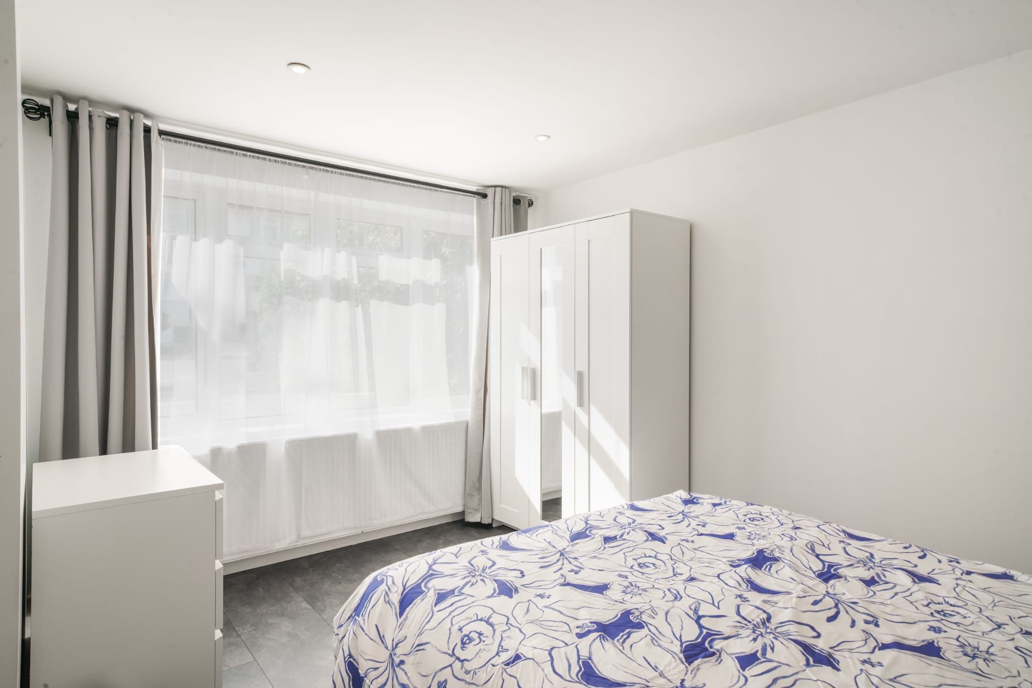 A bedroom with a bed, a wardrobe, a desk, and a window with curtains.