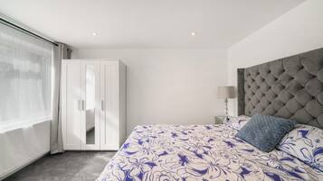 A bedroom with a large bed, a wardrobe, a bedside table with a lamp, and a view through a window.