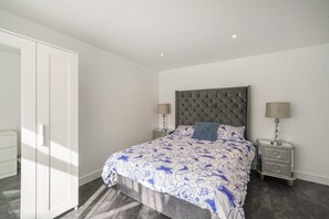 Un dormitorio con cama, dos mesitas de noche, un armario y una lámpara en el techo.