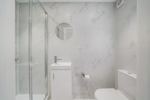 A modern bathroom with a glass-enclosed shower, a sink with a mirror, and a toilet. - Ground Floor Flat with Garden & Parking (London)