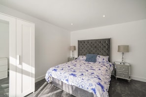 A bedroom with a bed, two bedside tables, a wardrobe, and a ceiling light. - Ground Floor Flat with Garden & Parking (London)