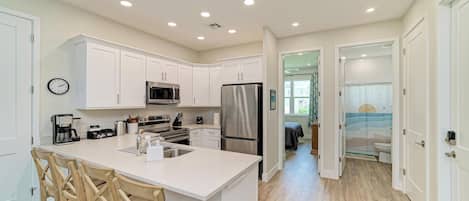 A modern kitchen with white cabinetry, stainless steel appliances, and a central island with seating.