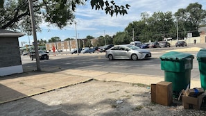 Ein Parkplatz mit Autos, einem Gebäude und grünen Müllbehältern.