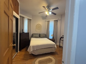 Ein Schlafzimmer mit einem Bett, einem Schminktisch, einem Deckenventilator und einem Traumfänger an der Wand.