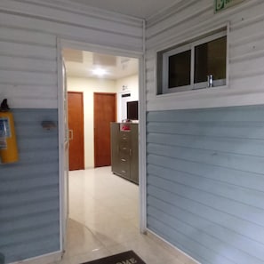 Een gang met een deur naar een kamer, een brandblusser en een raam met uitzicht.