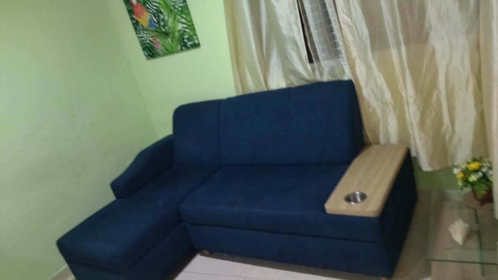 Un sofá azul con una mesita de madera en una habitación con pared verde y una ventana con cortinas blancas.