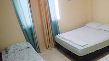 Una habitación con dos camas, una ventana con cortinas, un equipo de aire acondicionado y piso de baldosas.