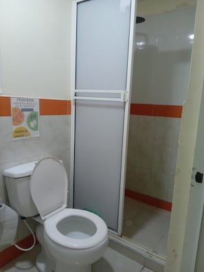 Een badkamer met toilet, douchecabine en een bordje aan de muur.