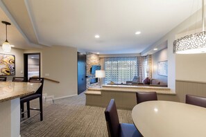 A modern hotel room with a dining area, a living space with a sofa and a TV, and a stone accent wall. - Stagecoach 2027 Rental at Marriott's Desert Villas I 2 Bedroom with full kitchen (Palm Desert)