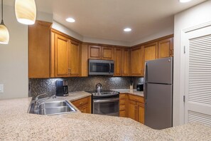 Una cocina con armarios de madera, un refrigerador de acero inoxidable, un microondas, una cafetera y una estufa a gas.