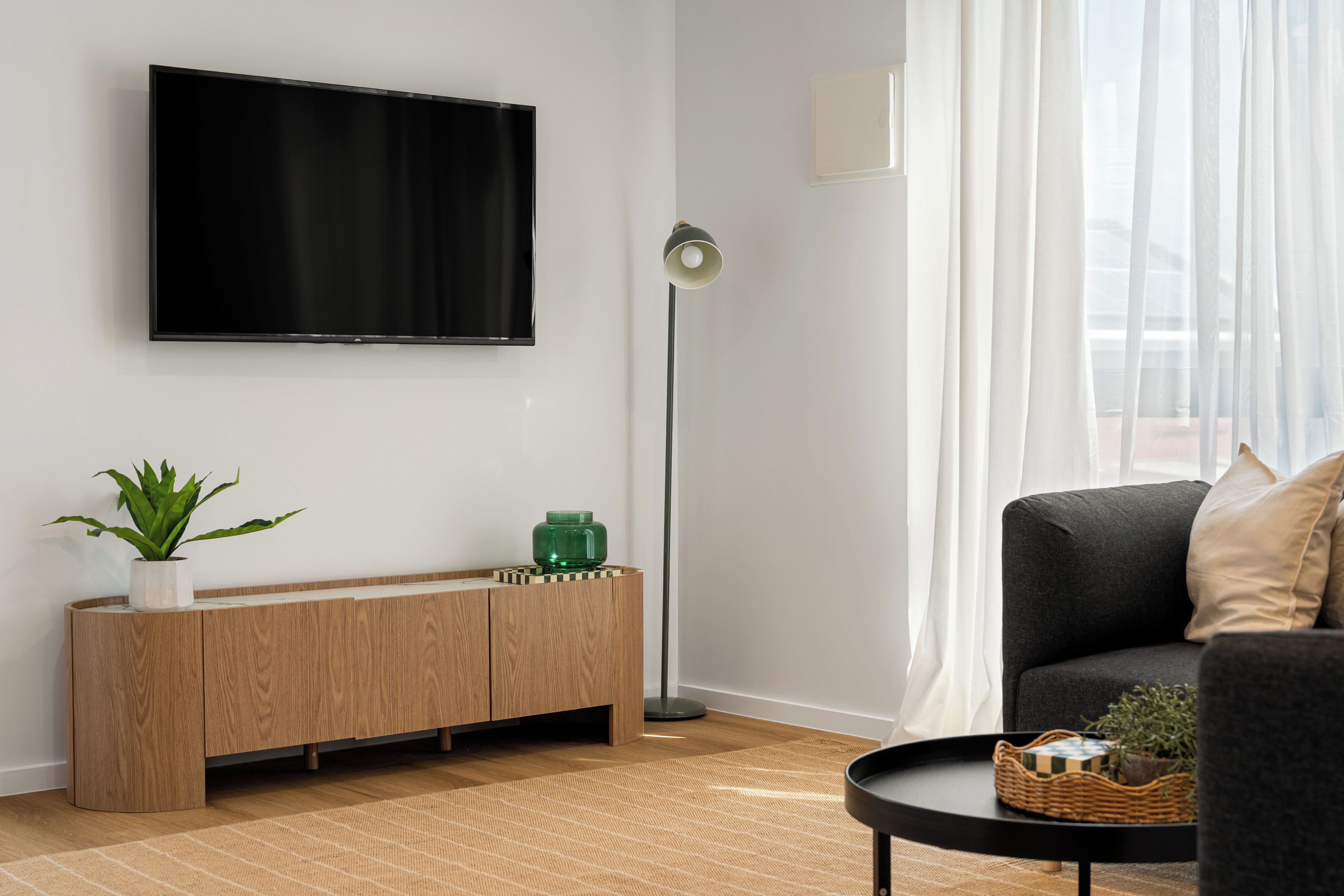 A modern living room with a flat-screen TV, a wooden console, a floor lamp, and a sofa.