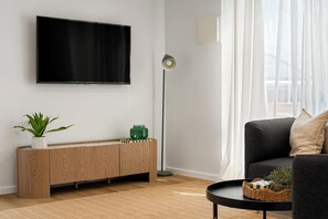 A modern living room with a flat-screen TV, a wooden console, a floor lamp, and a sofa.