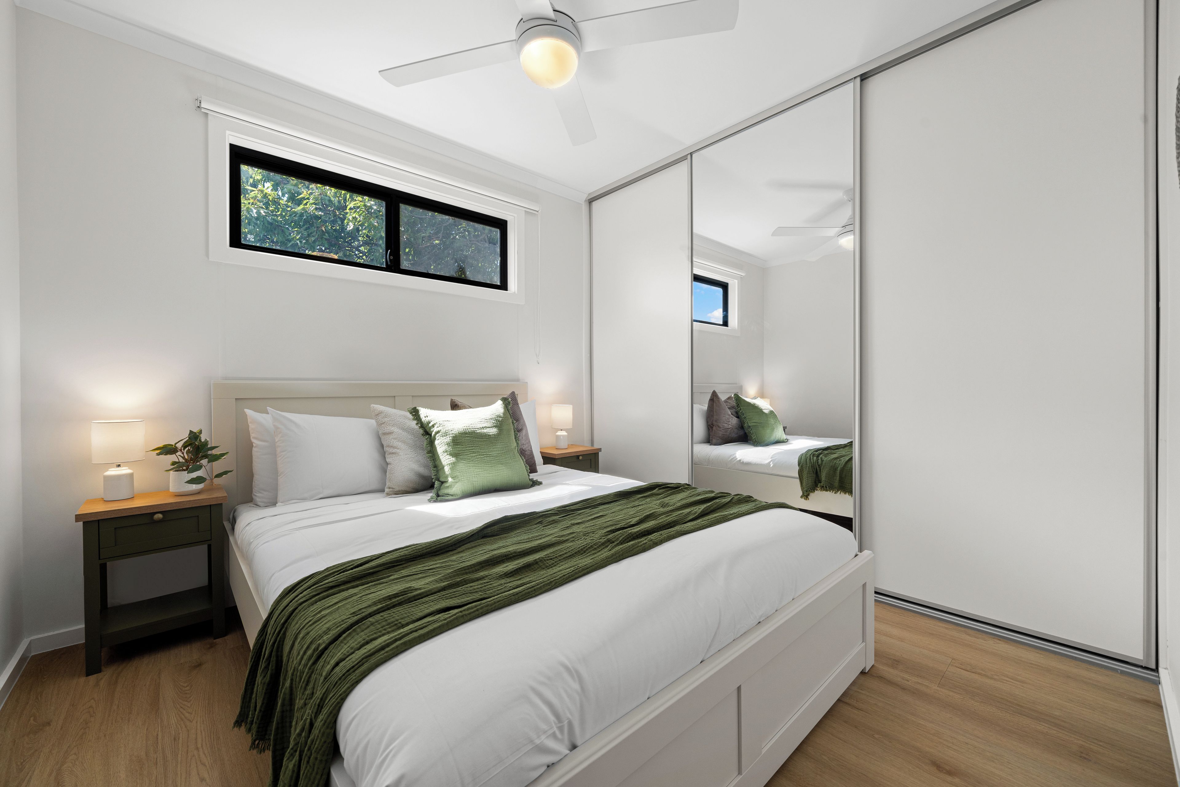 A bedroom with a bed, bedside tables, a nightstand, a window, and a ceiling fan.