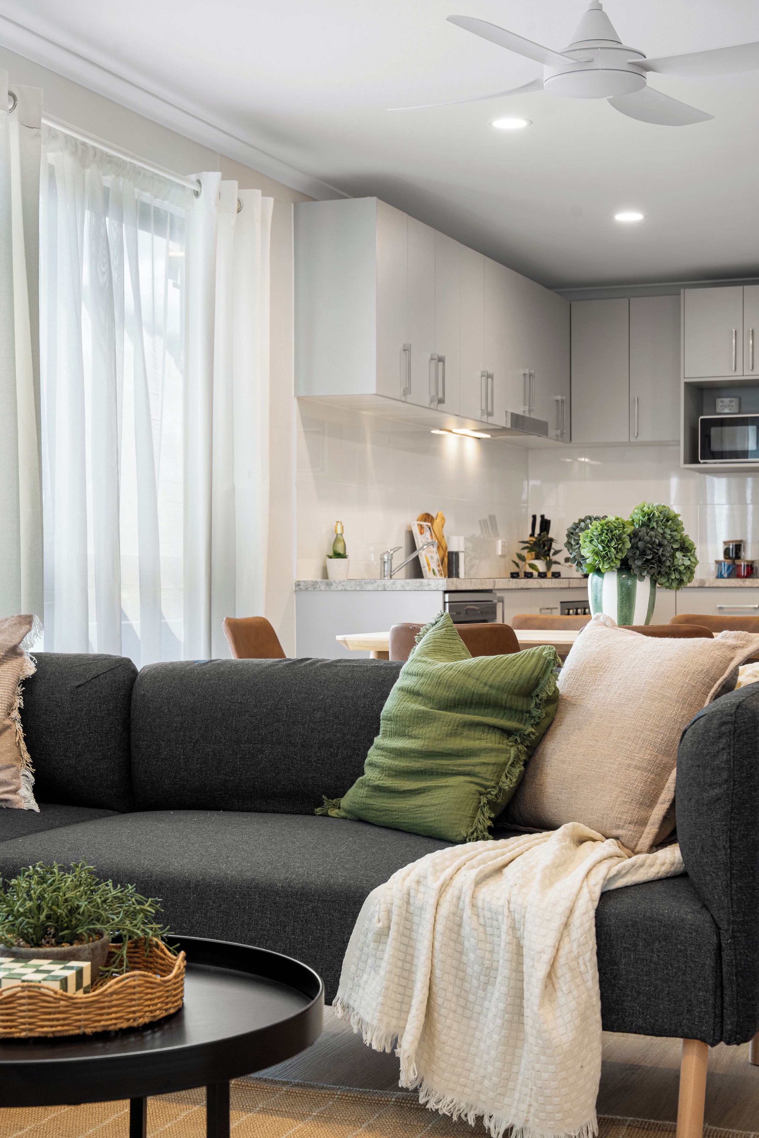 A modern living room with a grey sofa, a round coffee table, and a ceiling fan.