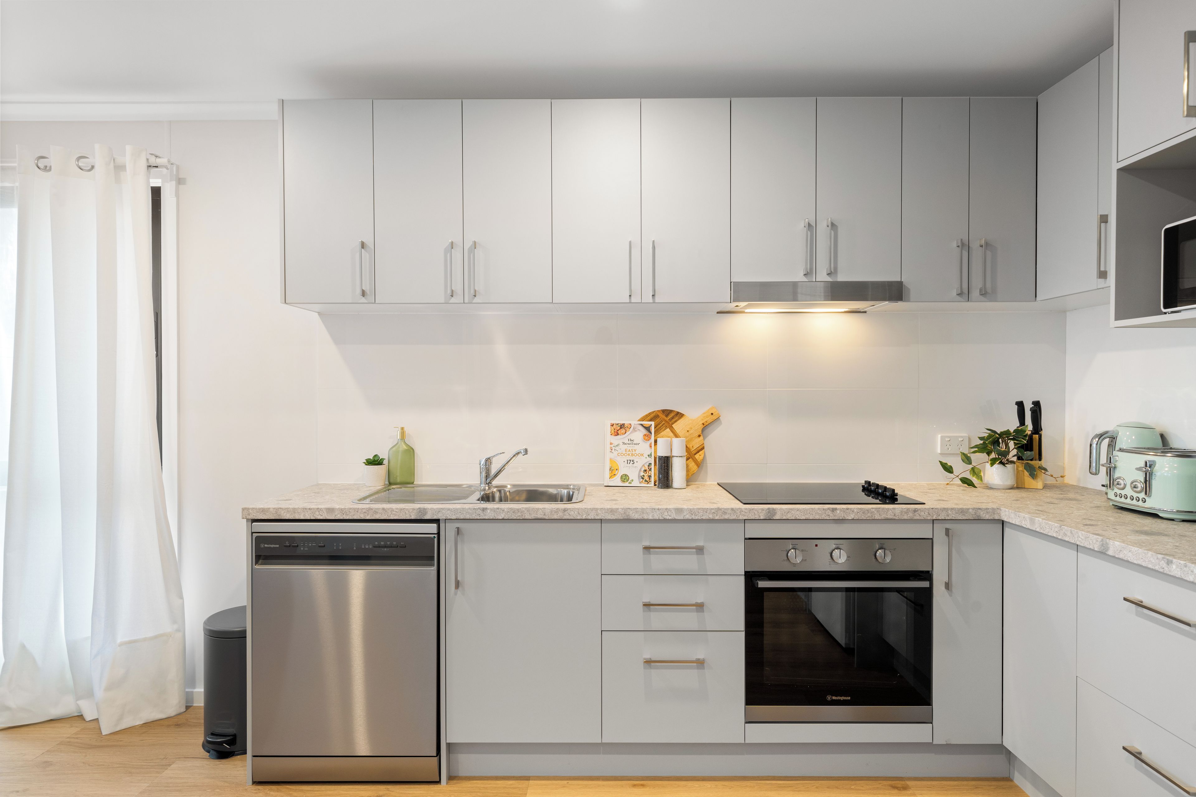A modern kitchen with grey cabinets, stainless steel appliances, and a marble countertop.