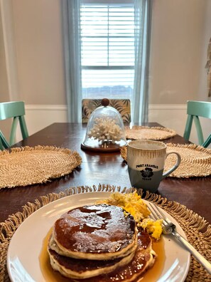 A dining table with a plate of pancakes, a mug, and a decorative item. - Walk to Beach in 15 mins! Shared Pool/Spa! 3b/3.5b. (Port Aransas)