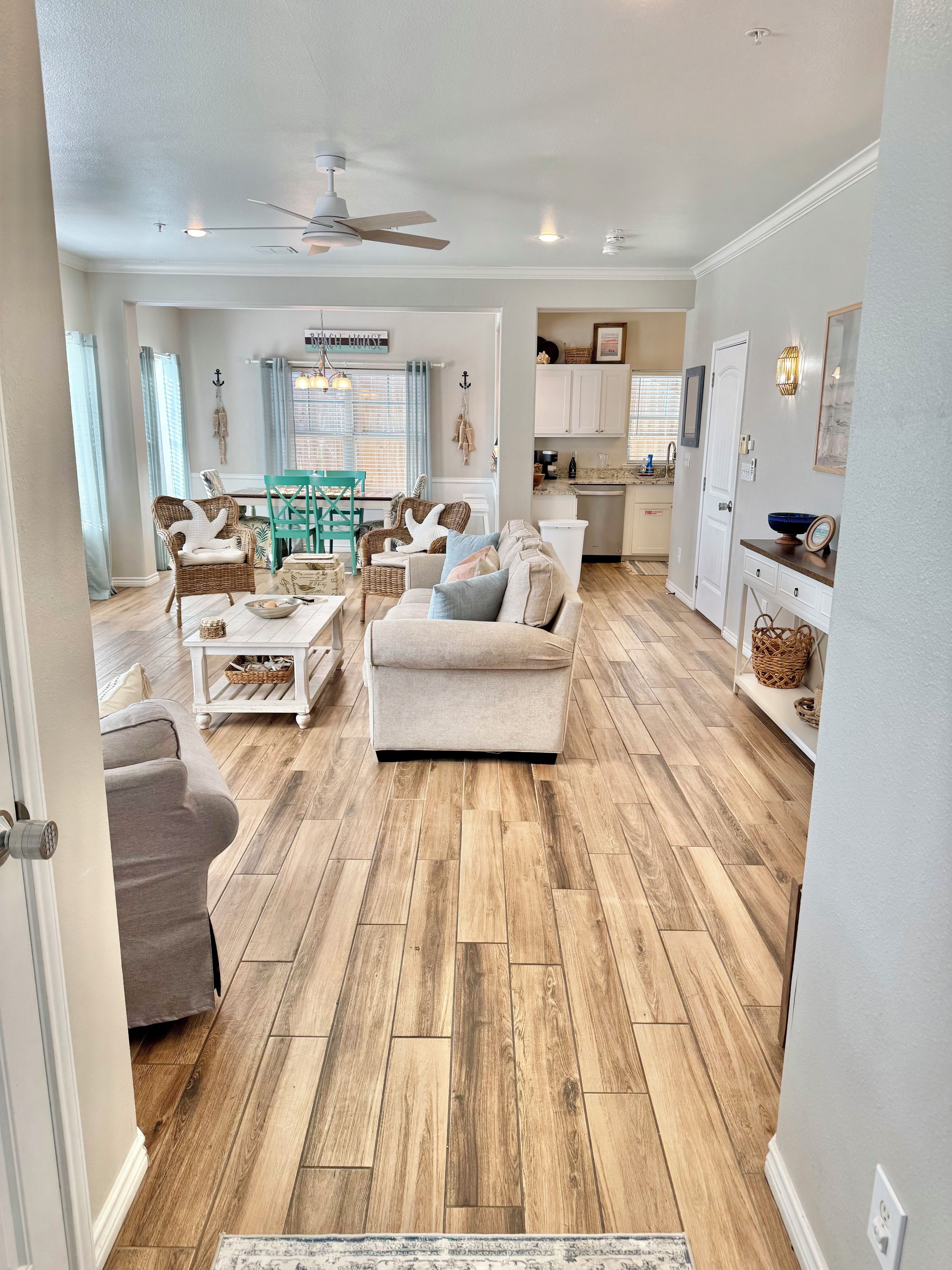 A spacious living room with a wooden floor, a ceiling fan, and a dining area with a table and chairs.