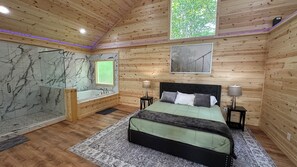 A wooden cabin bedroom with a large bed, a built-in bathtub, and a shower. - Where Peace Meets the Pines (Cleveland)