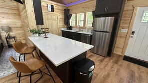 A modern kitchen with a central island, dark cabinets, stainless steel appliances, and wooden walls. - Where Peace Meets the Pines (Cleveland)