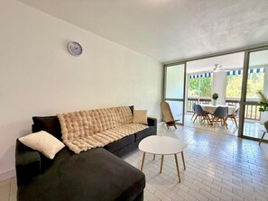 Ein modernes Wohnzimmer mit einem schwarzen Sofa, einem kleinen runden Tisch und einer großen Schiebeglastür, die zu einem Essbereich im Freien führt.