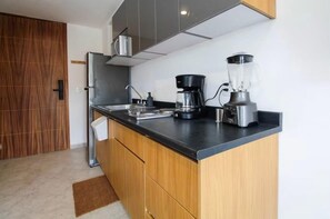 Una cuina compacta amb taulell negre, cafetera, batedora i nevera d'acer inoxidable.
