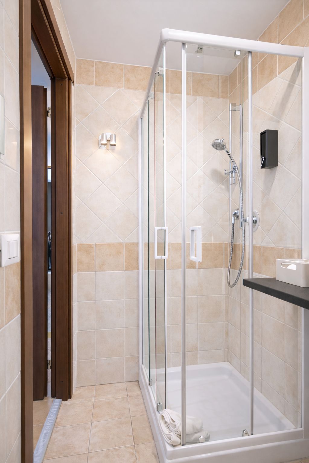 Eine begehbare Dusche mit Glastür, einer Handbrause und einer Bedienfeld an der Wand.