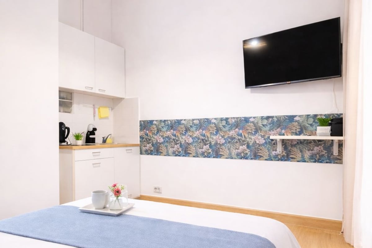 Ein modernes Schlafzimmer mit Bett, einem an der Wand befestigten Fernseher, einer Küchenzeile mit Schränken und einer dekorativen Spritzschutzwand.