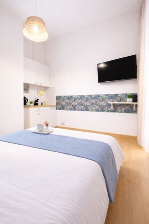 Ein modernes Schlafzimmer mit Bett, einem an der Wand befestigten Fernseher, einer Küchenzeile mit Schränken und einer dekorativen Spritzschutzwand.
