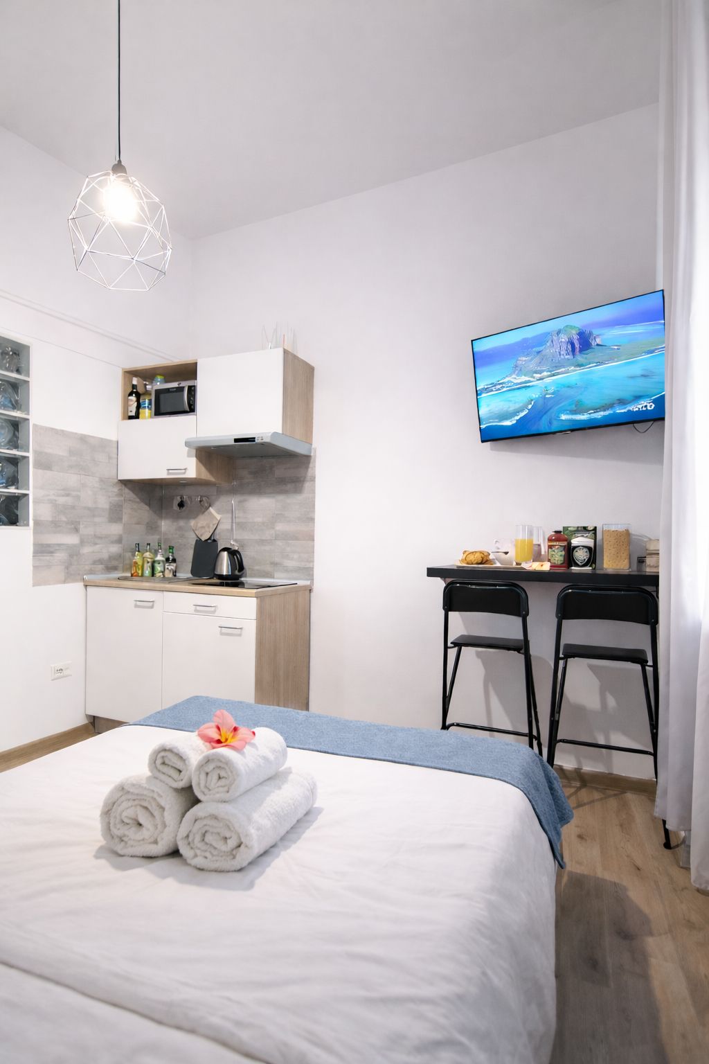 Una habitación de hotel moderna con cama, escritorio, televisor y kitchenette.