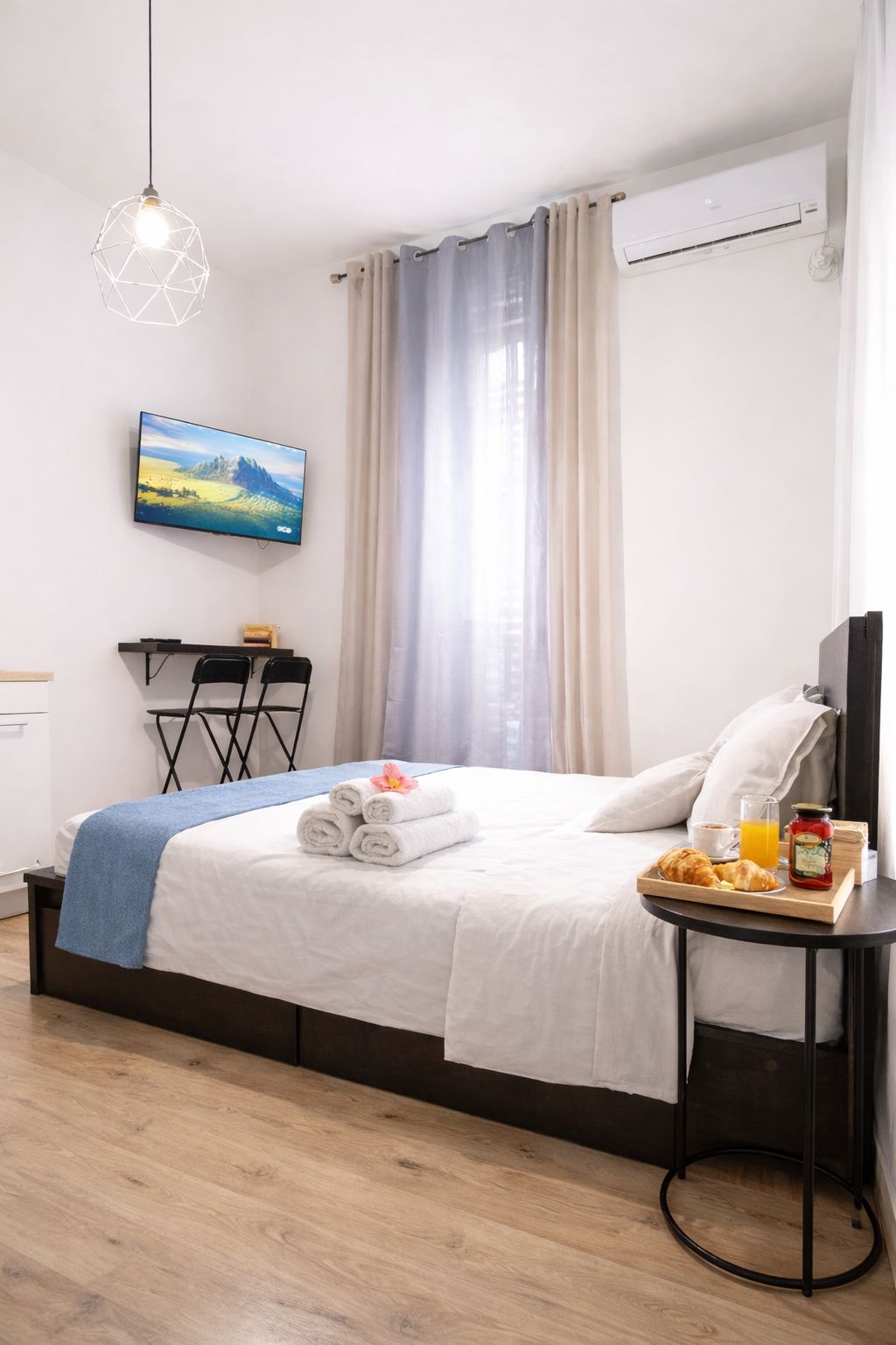 A hotel room with a bed, a TV, a small table with breakfast items, and a window with curtains.