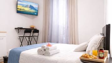 A hotel room with a bed, a TV, a small table with breakfast items, and a window with curtains.