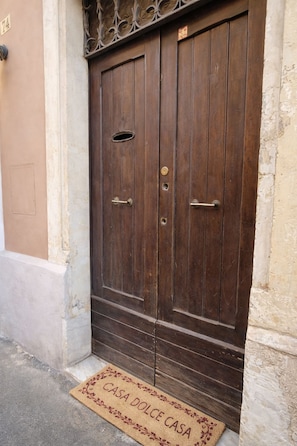 Puerta doble de madera con manija de latón y felpudo que reza 'CASA DOLCE CASA' en la entrada.