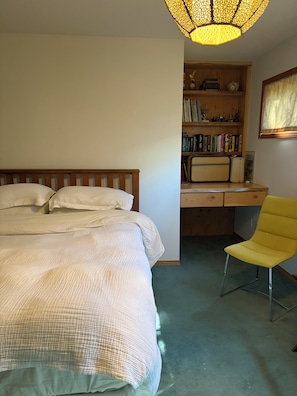 A bedroom with a bed, a desk with books, a chair, and a unique ceiling light fixture.