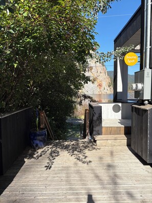 A wooden deck leading to a sauna area with a view of a cliff and a body of water.