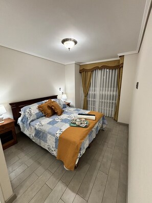 Un letto rifatto con una coperta a motivi, un comodino con una lampada e una finestra con tende.