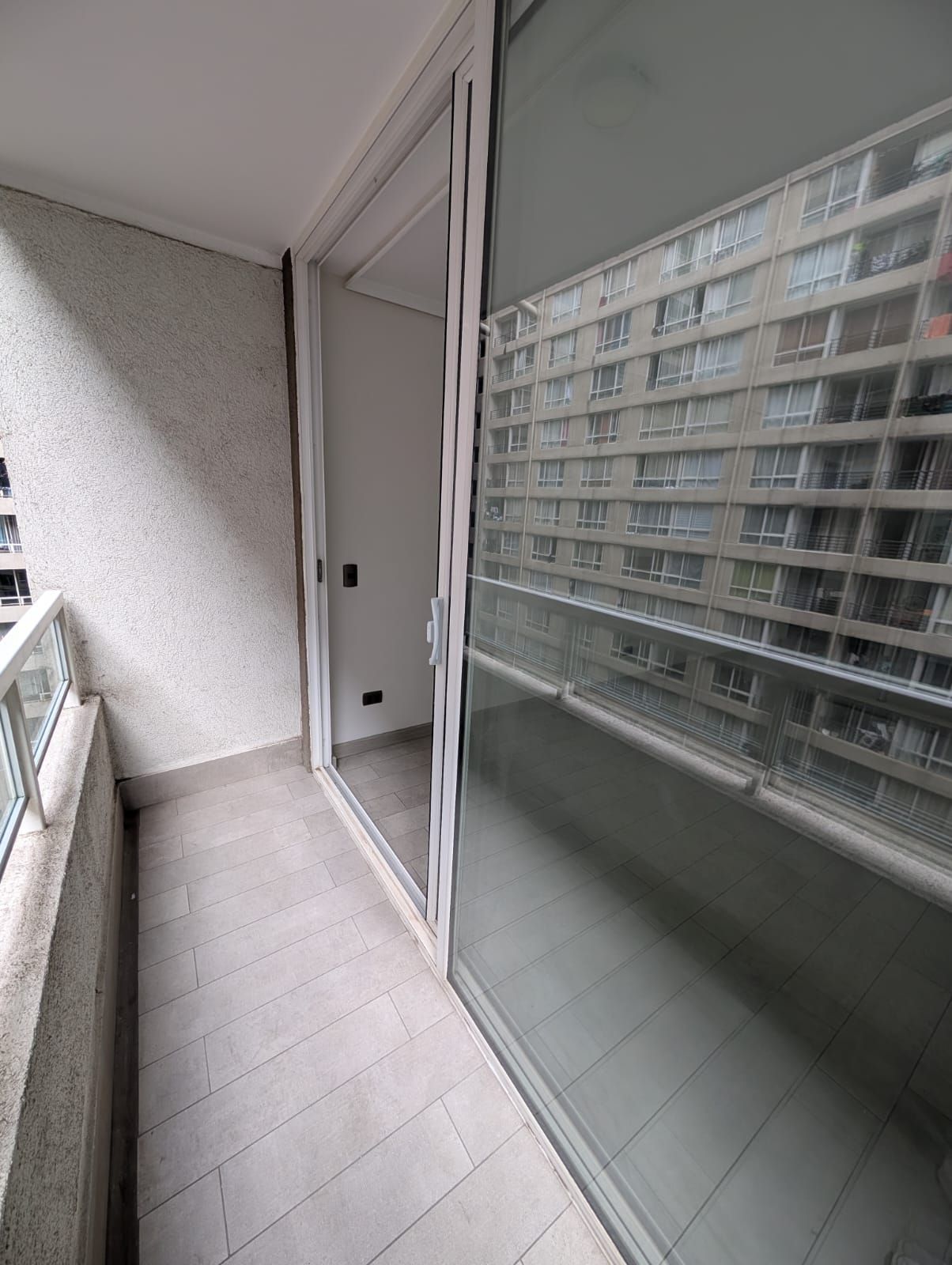 A balcony with a glass door leading to a building with multiple windows.