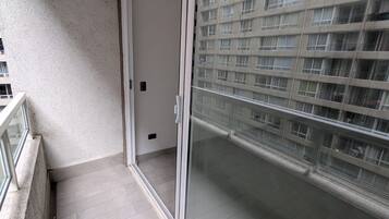 A balcony with a glass door leading to a building with multiple windows.