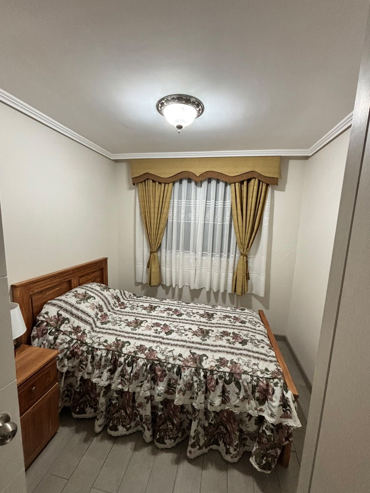A bedroom with a bed, curtains, a nightstand, and a ceiling light.