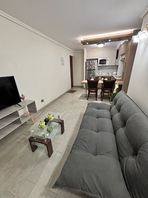 Sala de estar com sofá, mesa de centro e televisão. Cozinha compacta com micro-ondas e armários.