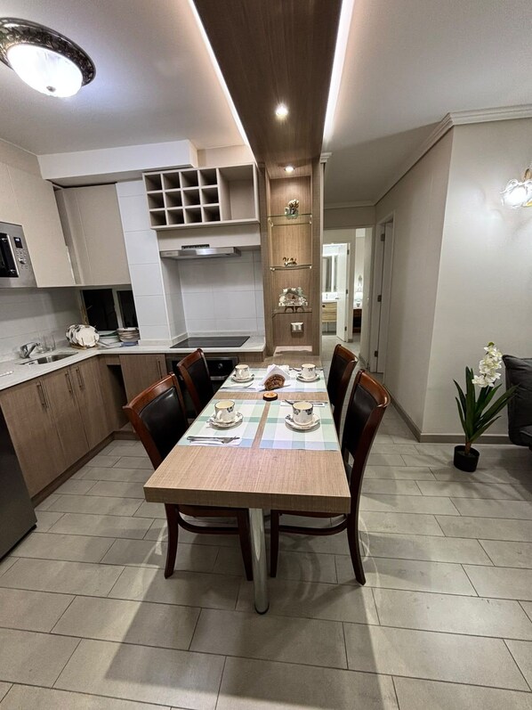 Een moderne keuken met een eethoek, met een lange houten tafel voor vier personen, compleet met stoelen en een kleine potplant.