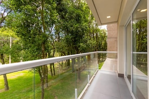A modern balcony with glass railings overlooking a grassy area with trees. - Vêneto Baldanho 101 (Gramado)