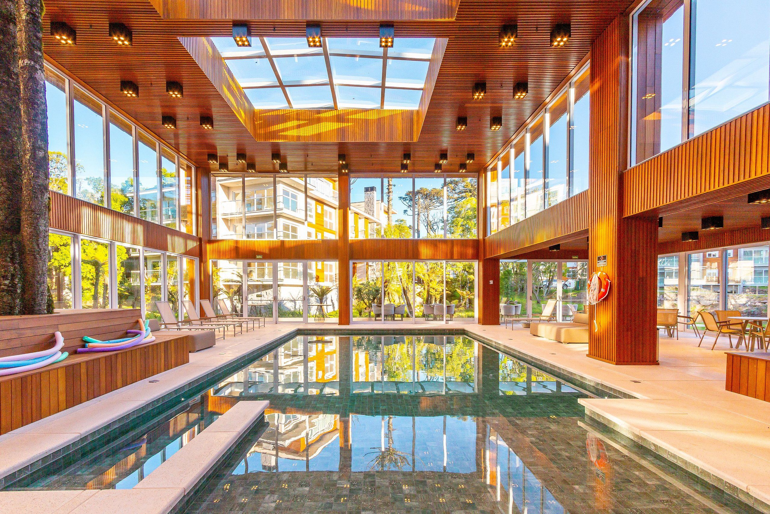 Un área de piscina interior moderna con paredes de vidrio, vigas de madera y una piscina central.