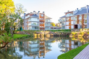 A modern apartment building with multiple floors, large windows, and a small water feature in front. - Vêneto Baldanho 101 (Gramado)