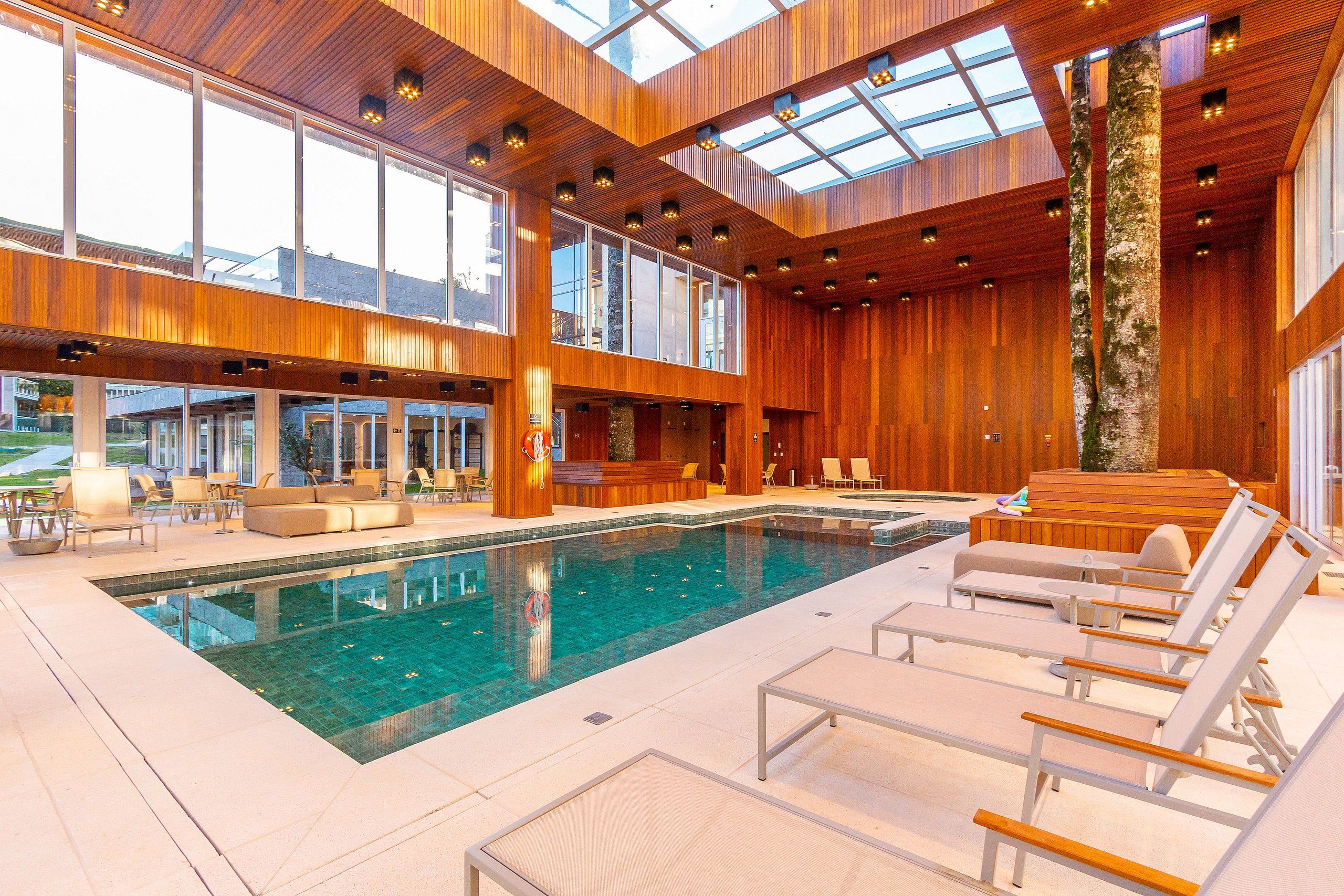 Uma área interna de piscina moderna com uma piscina grande, cadeiras de descanso e painéis de madeira.