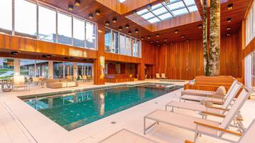 Uma área interna de piscina moderna com uma piscina grande, cadeiras de descanso e painéis de madeira.