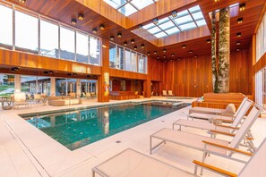 Uma área interna de piscina moderna com uma piscina grande, cadeiras de descanso e painéis de madeira.