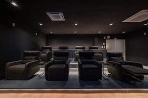 A home theater room with six black leather recliner chairs, a ceiling projector, and a door labeled 'SAIDA'. - Vêneto Baldanho 101 (Gramado)