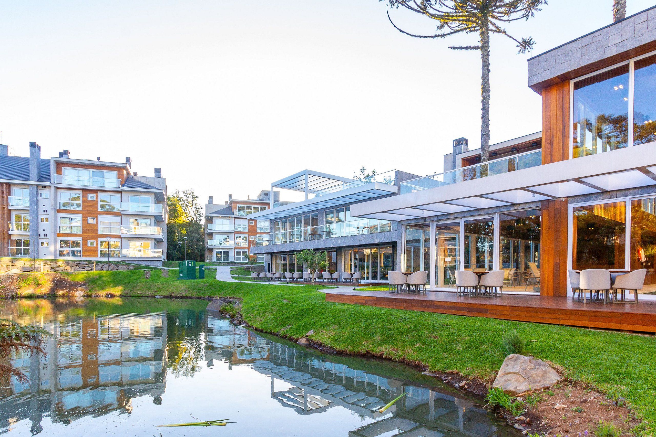 Un moderno edificio residencial con fachada de vidrio, zona de estar al aire libre y un pequeño estanque.